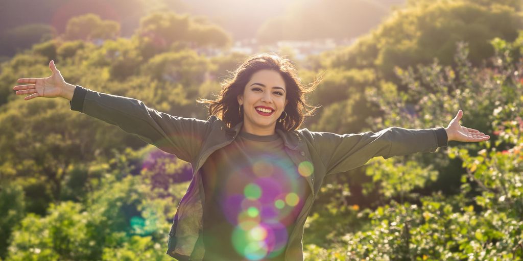 Confident individual in nature with open arms and smile.
